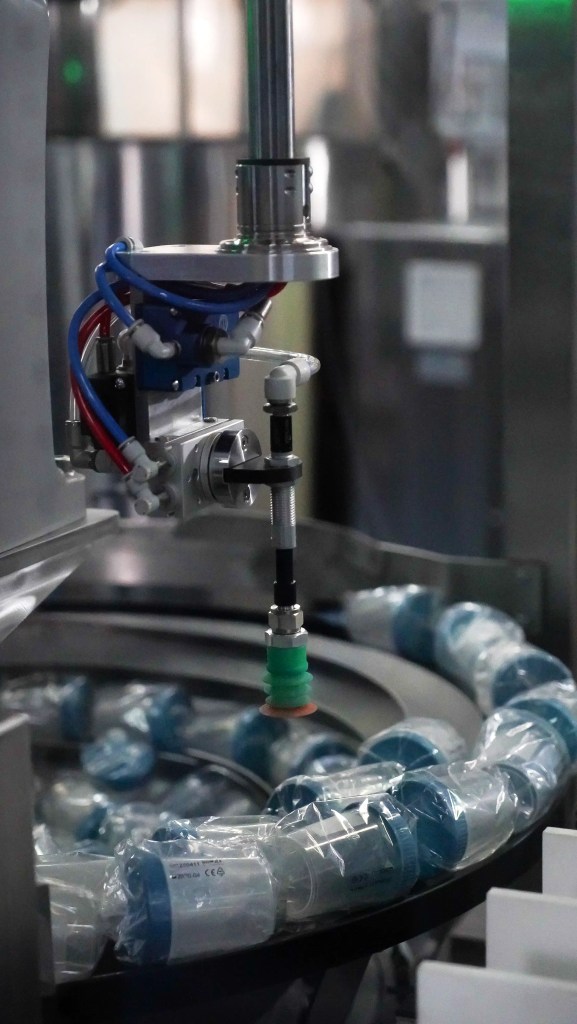 Overhead view of robotic end-of-line packaging cell sorting bottles from a circular feeder to a conveyor