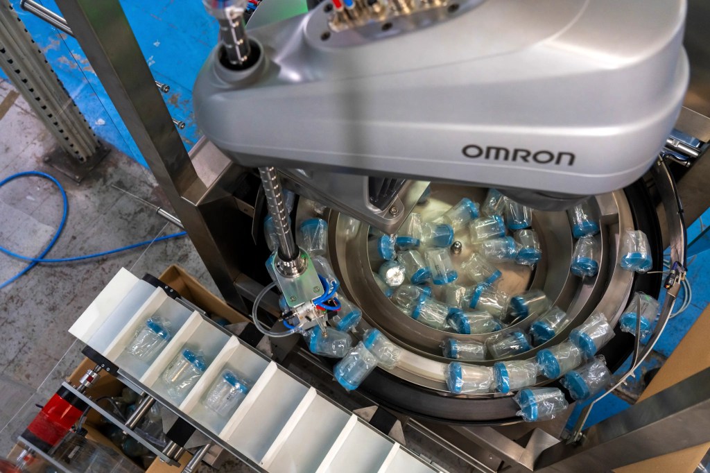 Robotic pick-and-place unit transferring bottles into conveyor lanes