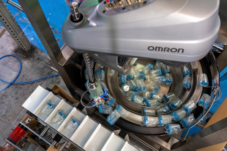 Robotic pick-and-place unit transferring bottles into conveyor lanes